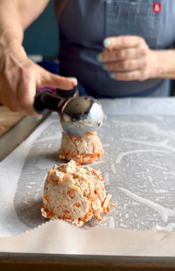 carrot biscuit dough being placed on a baking sheet